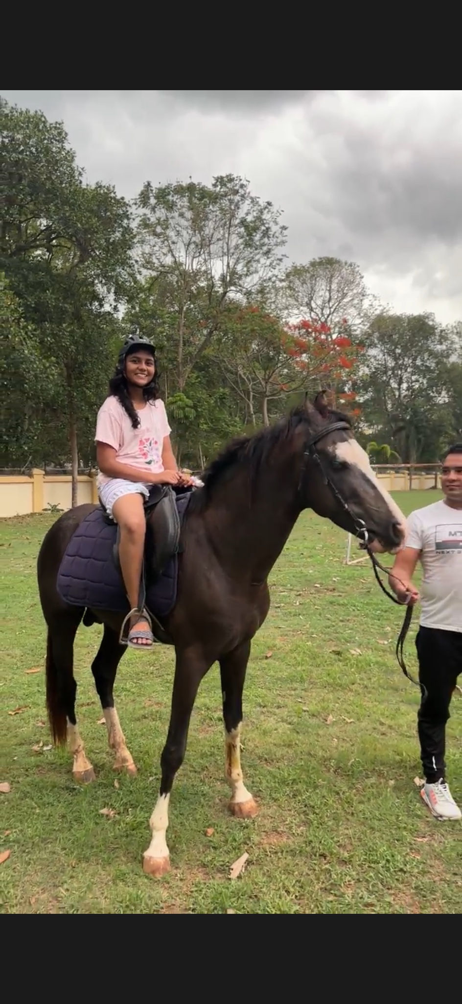 A helmeted camper riding a black horse with a handler nearby.