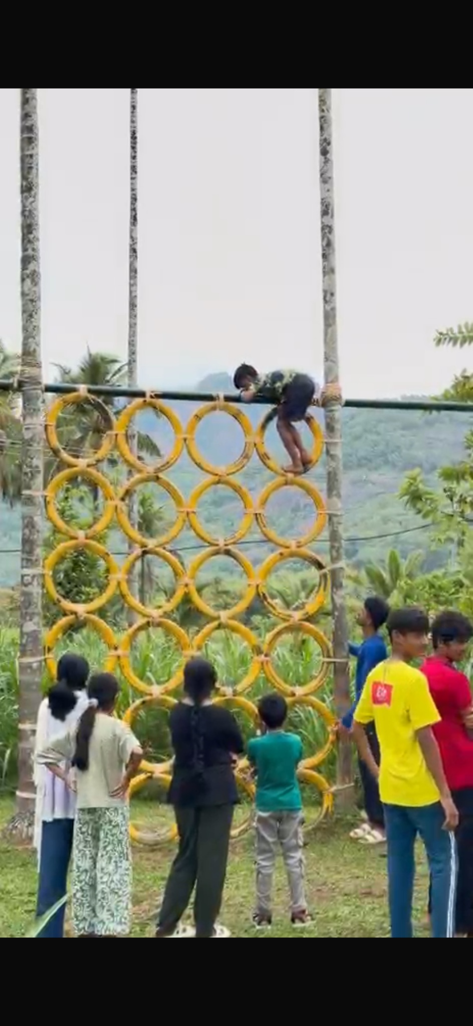Campers encouraging a participant climbing a yellow tyre wall.