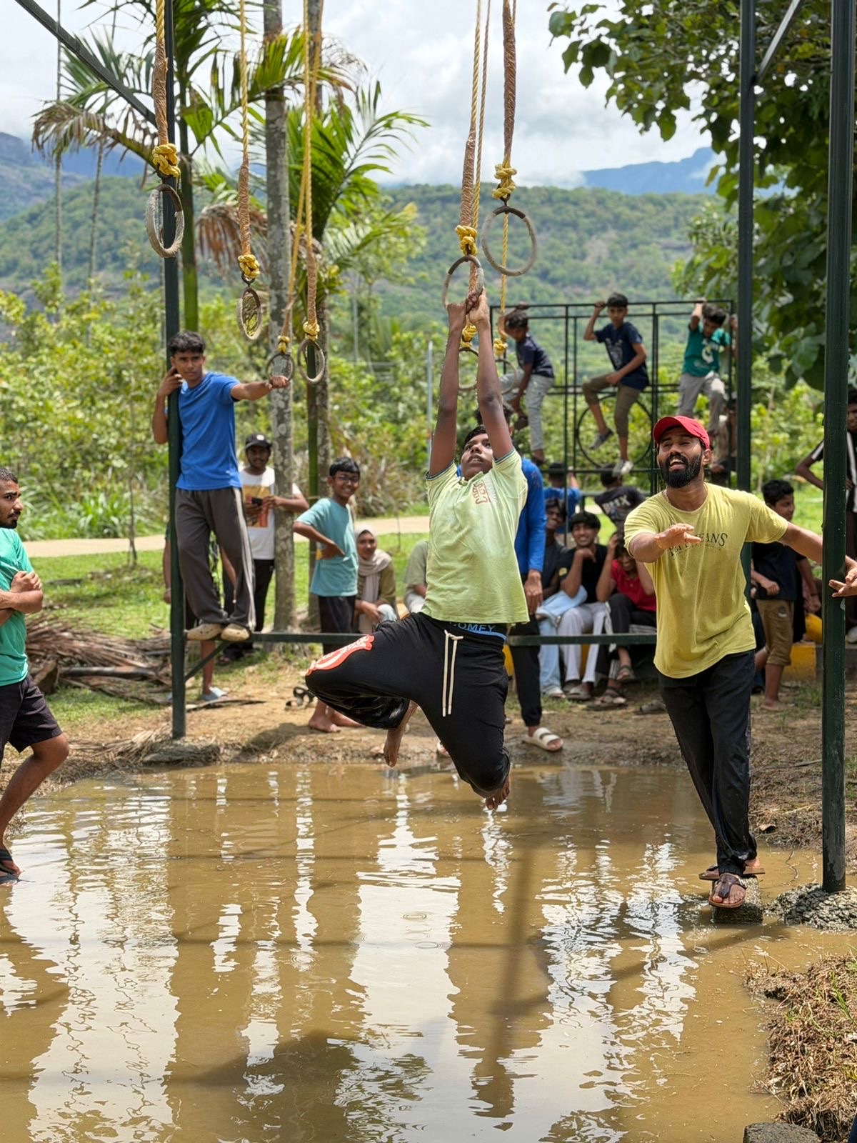 A camper using hanging rings above water with a facilitator alongside.