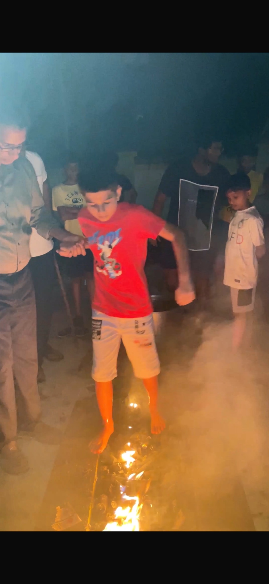 A camper taking part in an evening fire challenge with adults nearby.